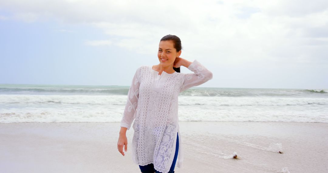 Woman enjoying beach in white tunic and smiling under cloudy sky - Free Images, Stock Photos and Pictures on Pikwizard.com