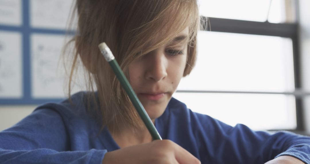 Young Student Writing with Pencil in Classroom