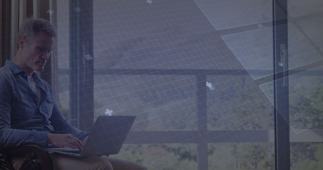 Mature man working remotely on laptop in lounge by paneled window with copy space