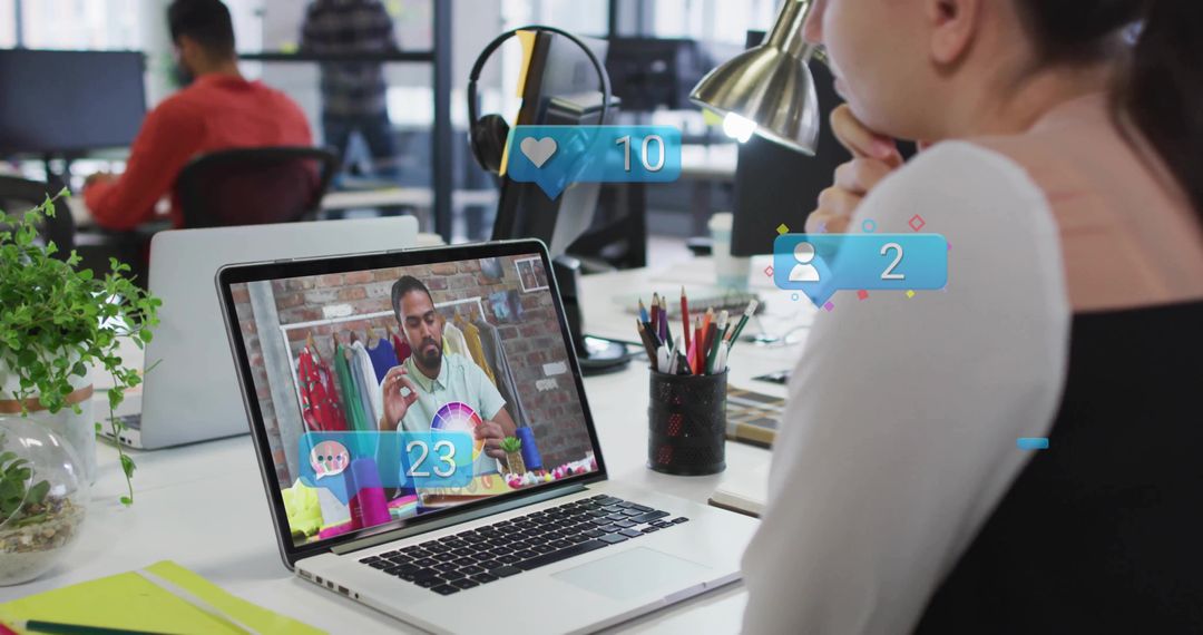 Woman viewing live color design tutorial on laptop in shared office with social overlays