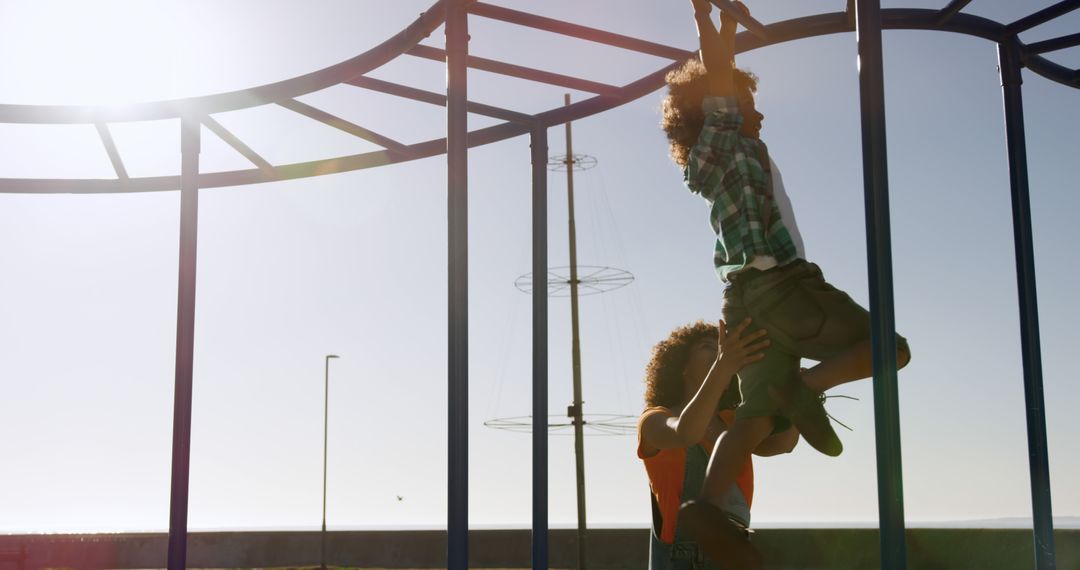 African American mother helping child on monkey bars at playground - Free Images, Stock Photos and Pictures on Pikwizard.com