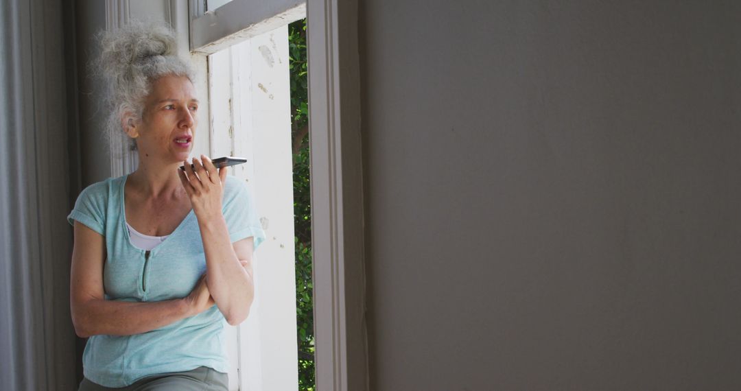 Elderly Woman Using Voice Assistant on Smartphone by Window - Free Images, Stock Photos and Pictures on Pikwizard.com