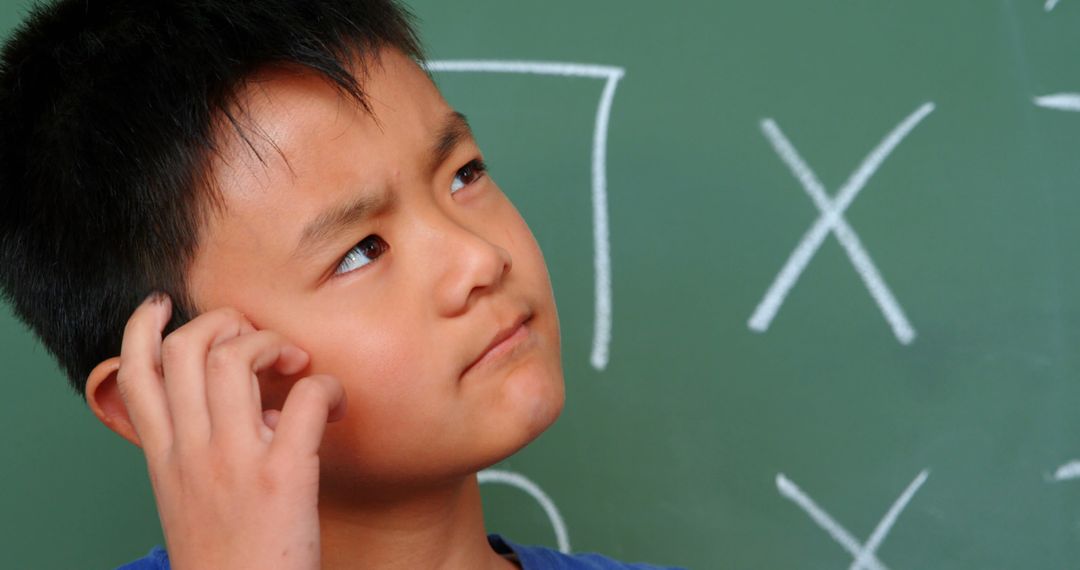 Thoughtful Boy Scratching Head Near Classroom Chalkboard