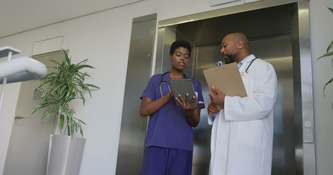 Medical Professionals Using Digital Tablet and Discussing Patient Records in Hospital Corridor - Free Images, Stock Photos and Pictures on Pikwizard.com