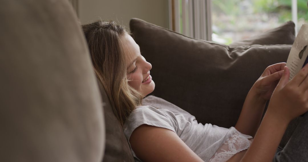 Girl Smiling While Reading on Comfortable Sofa - Free Images, Stock Photos and Pictures on Pikwizard.com