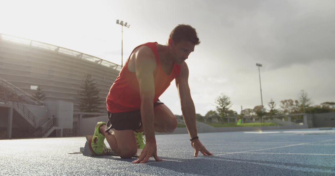 Sprinter preparing at starting blocks on blue track backlit under stadium lights