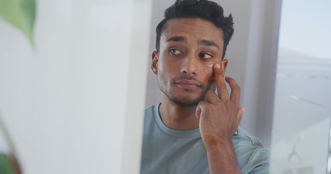 Young Man Applying Skincare Product to Face in Mirror - Free Images, Stock Photos and Pictures on Pikwizard.com