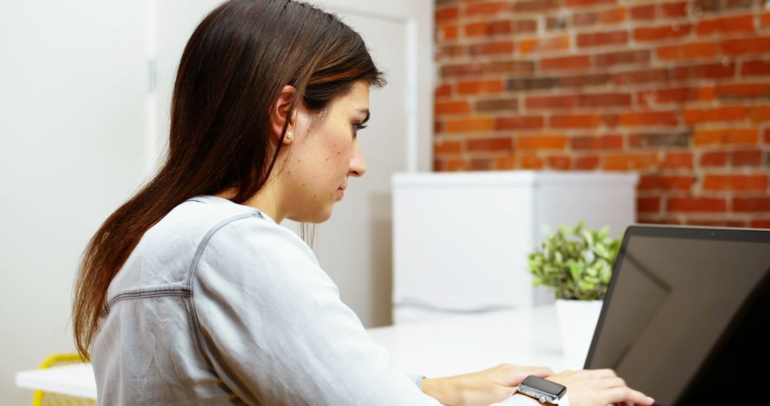 Young Woman Working on Laptop in Office with Exposed Brick Wall - Free Images, Stock Photos and Pictures on Pikwizard.com