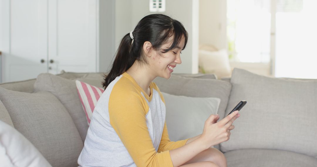 Smiling Woman Relaxing with Smartphone on Sofa