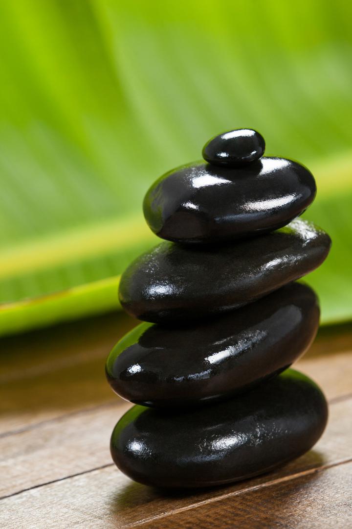 Stacked Black Pebble Stones on Wooden Surface with Green Leaf Background - Free Images, Stock Photos and Pictures on Pikwizard.com