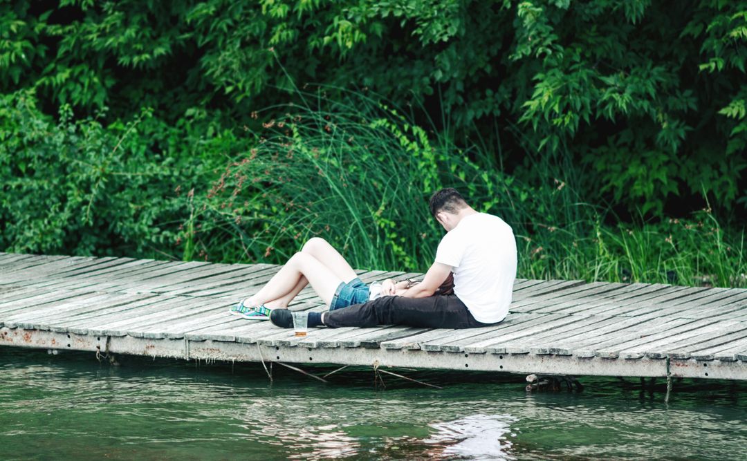 Couple Relaxing on Wood Dock by Lake Surrounded by Lush Greenery