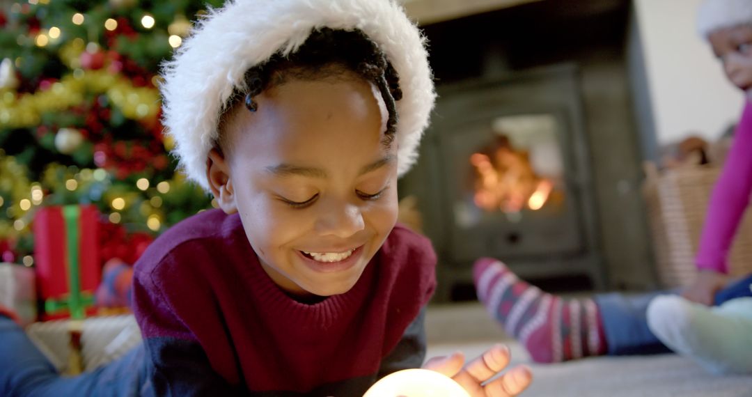 Boy Holding Christmas Decoration Smiling Prone by Fireplace - Free Images, Stock Photos and Pictures on Pikwizard.com