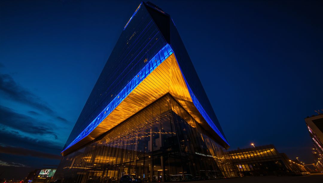 Triangular skyscraper glowing with warm overhang lighting and blue LED accents at night