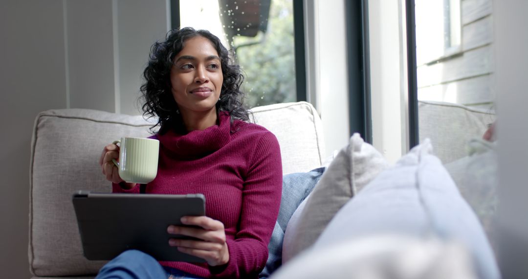 Woman Relaxing with Tablet and Mug on Couch by Large Window - Free Images, Stock Photos and Pictures on Pikwizard.com