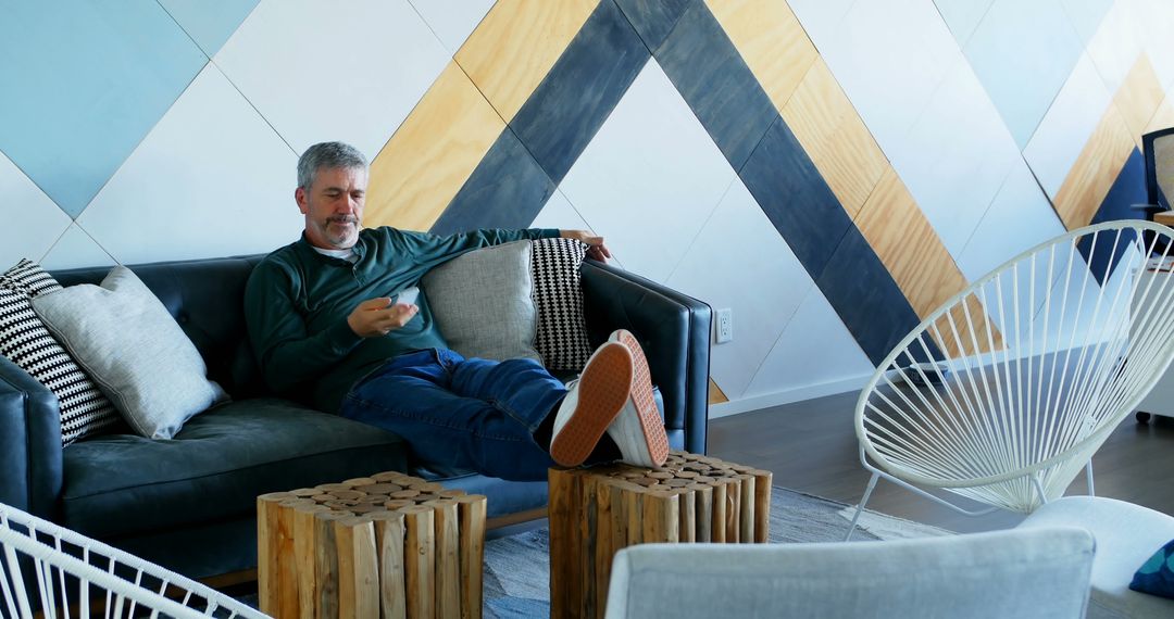 Man Relaxing on Sofa in Modern Living Room with Geometric Wall Design - Free Images, Stock Photos and Pictures on Pikwizard.com