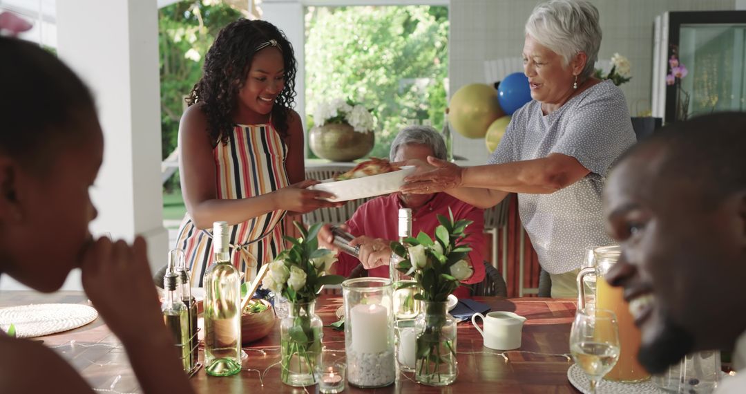 Multigenerational family sharing summer meal passing plate and smiling around dining table