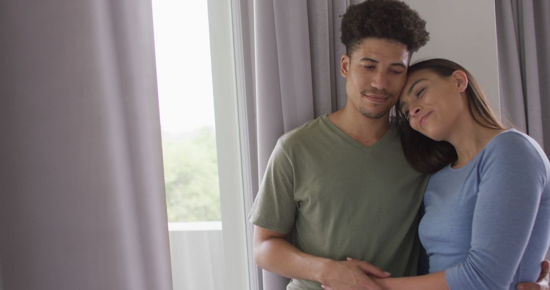 Interracial Couple Embracing Near Window at Home