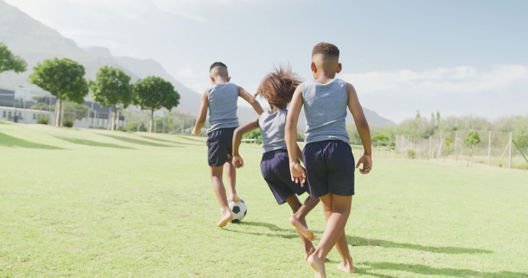 Image of three african american schoolchildren playing football barefoot in field - Free Images, Stock Photos and Pictures on Pikwizard.com