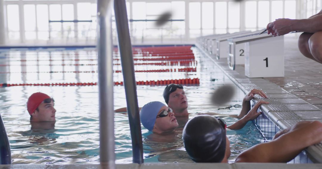 Competitive swimmers listening to coach at pool edge during indoor training session
