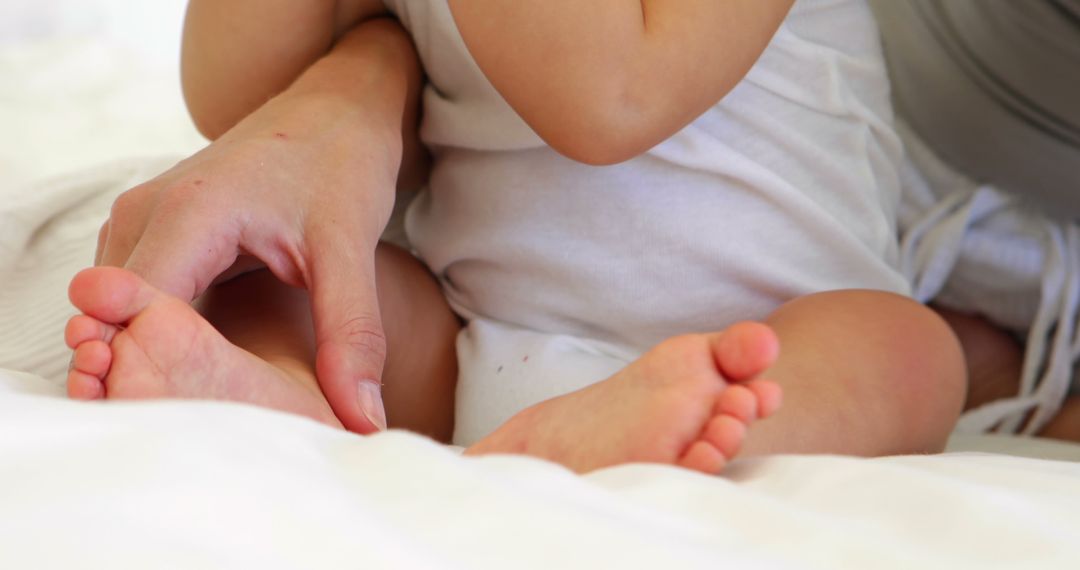 Mother touching her baby daughters toes at home in bedroom - Free Images, Stock Photos and Pictures on Pikwizard.com