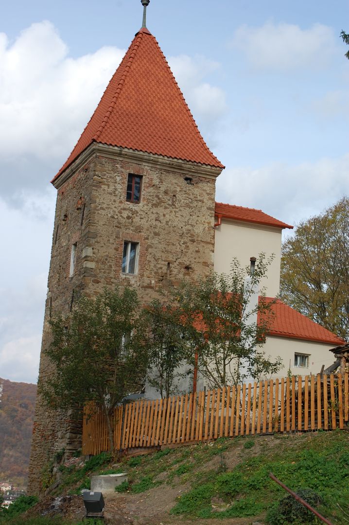 Medieval Stone Tower Standing with Red Tiled Roof and Wooden Fence on Hill