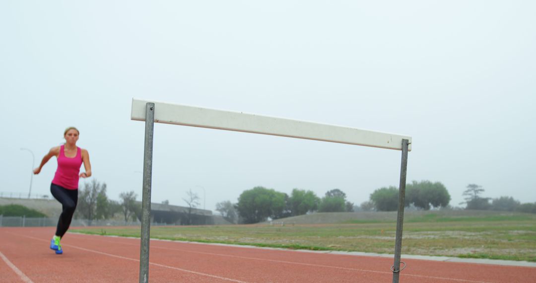 Female Athlete Training on Track Jumping Hurdle