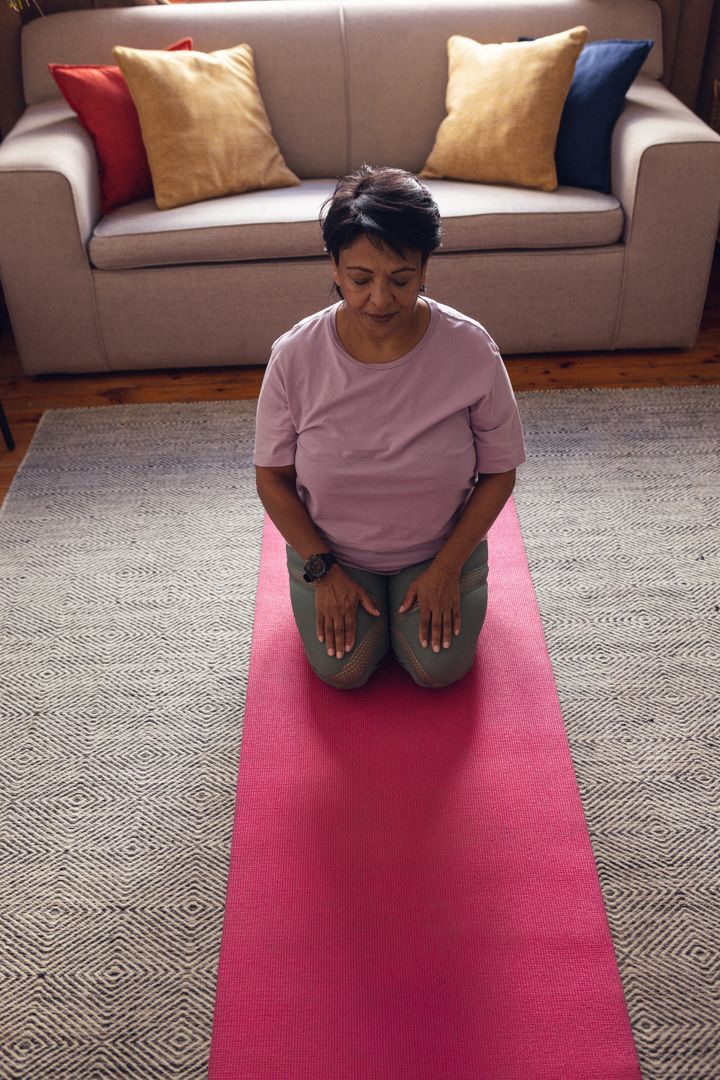 High angle view of biracial mature woman with eyes closed kneeling and meditating on mat at home - Free Images, Stock Photos and Pictures on Pikwizard.com