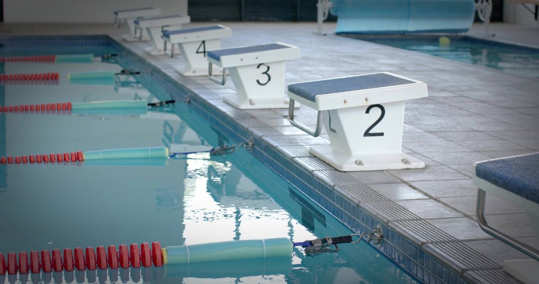 Starting blocks lined at indoor competition pool with lane ropes and water reflections