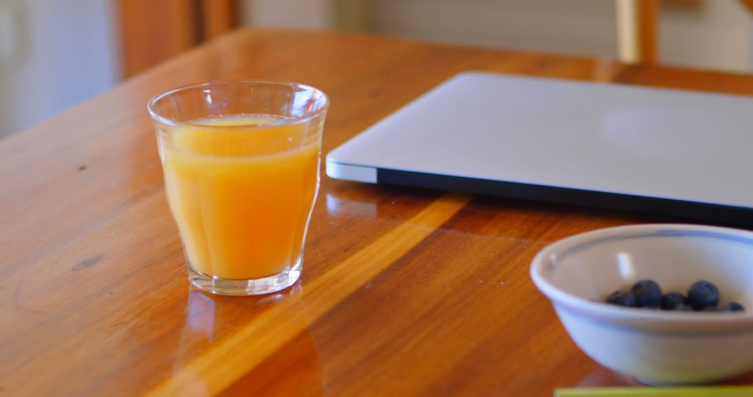 Glass of Fresh Orange Juice on Wooden Table with Laptop and Bowl of blueberries - Free Images, Stock Photos and Pictures on Pikwizard.com