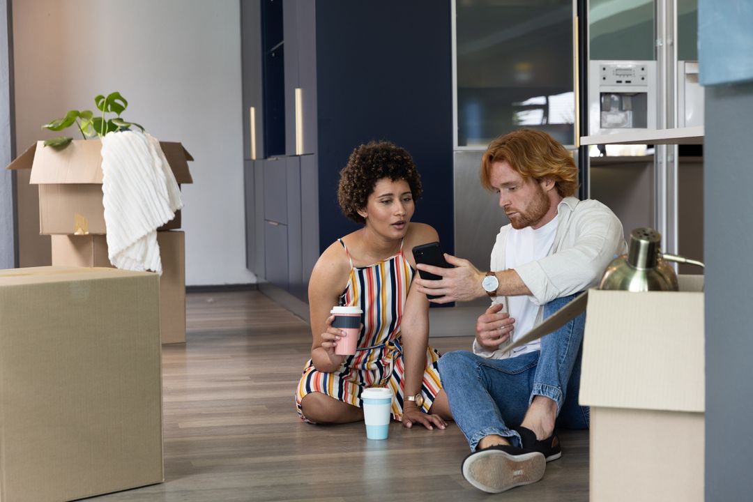 Diverse Couple Reviewing Smartphone in New Home with Moving Boxes