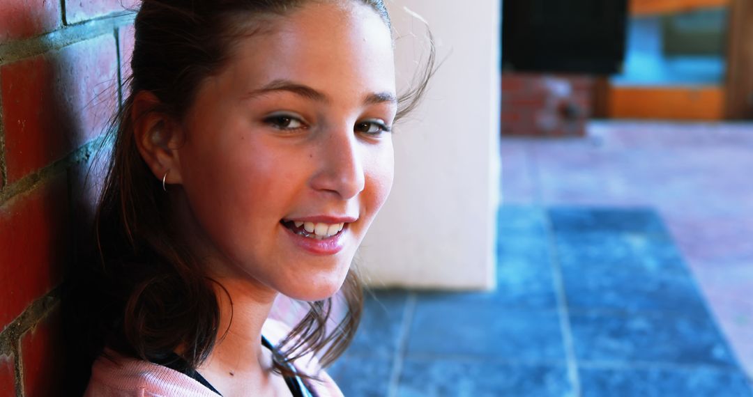 A young Caucasian girl leans against a brick wall, smiling gently, with copy space - Free Images, Stock Photos and Pictures on Pikwizard.com