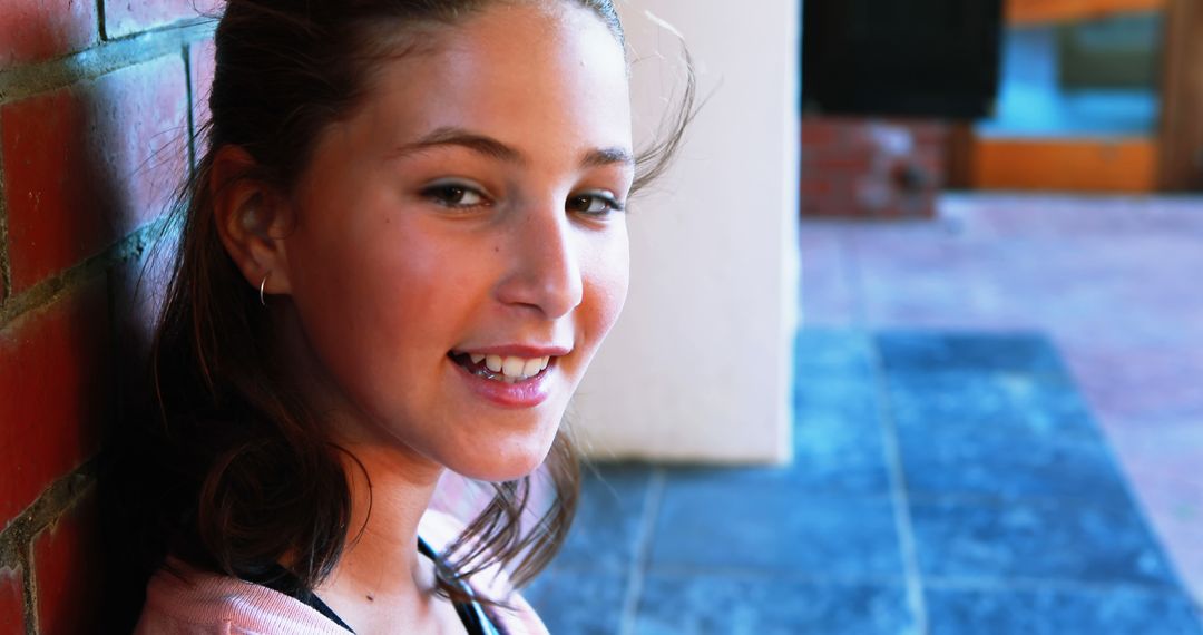 Smiling Teenage Girl Leaning on Brick Wall Outdoors - Free Images, Stock Photos and Pictures on Pikwizard.com