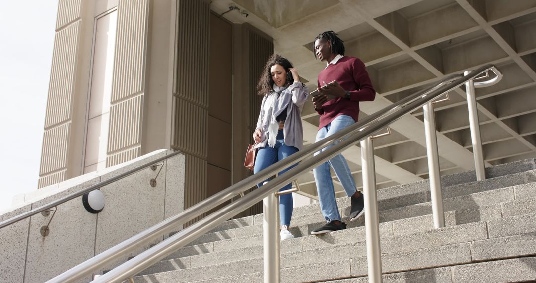 Multiracial college students walking down campus steps holding tablet and bag