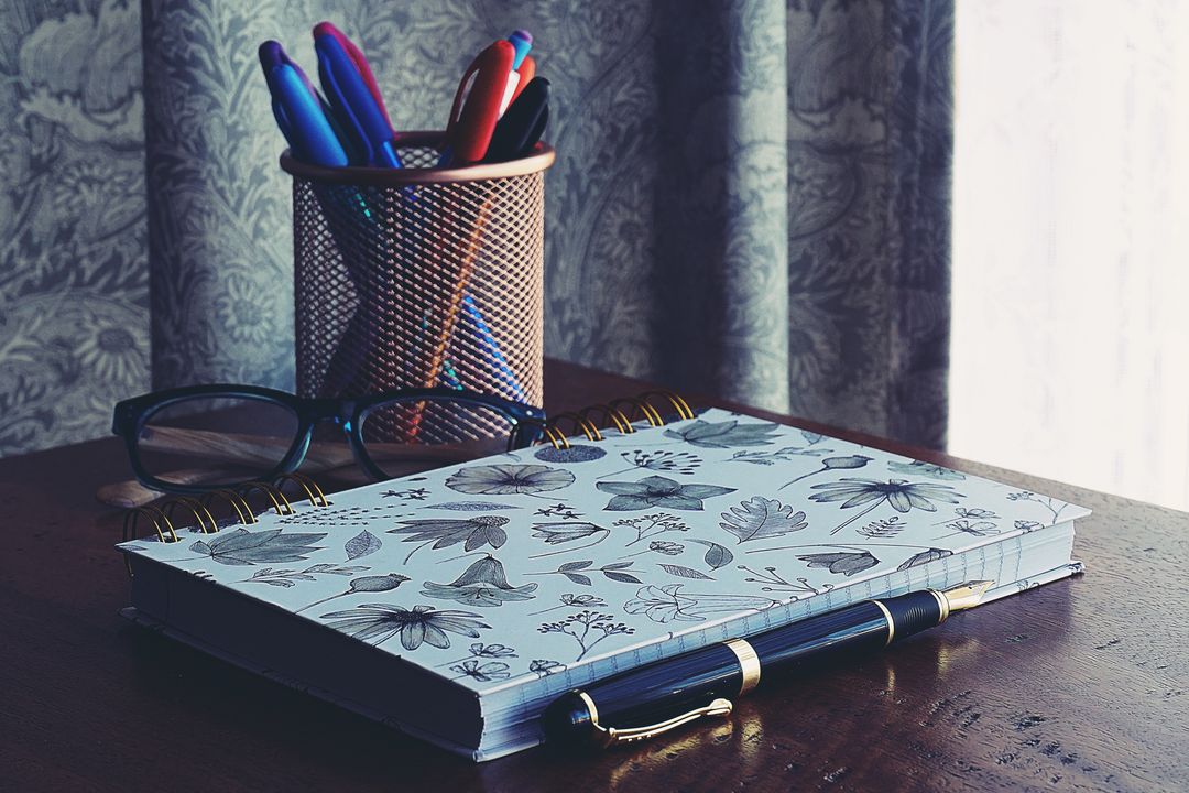 Creative workspace with journal, book, and writing pens on desk