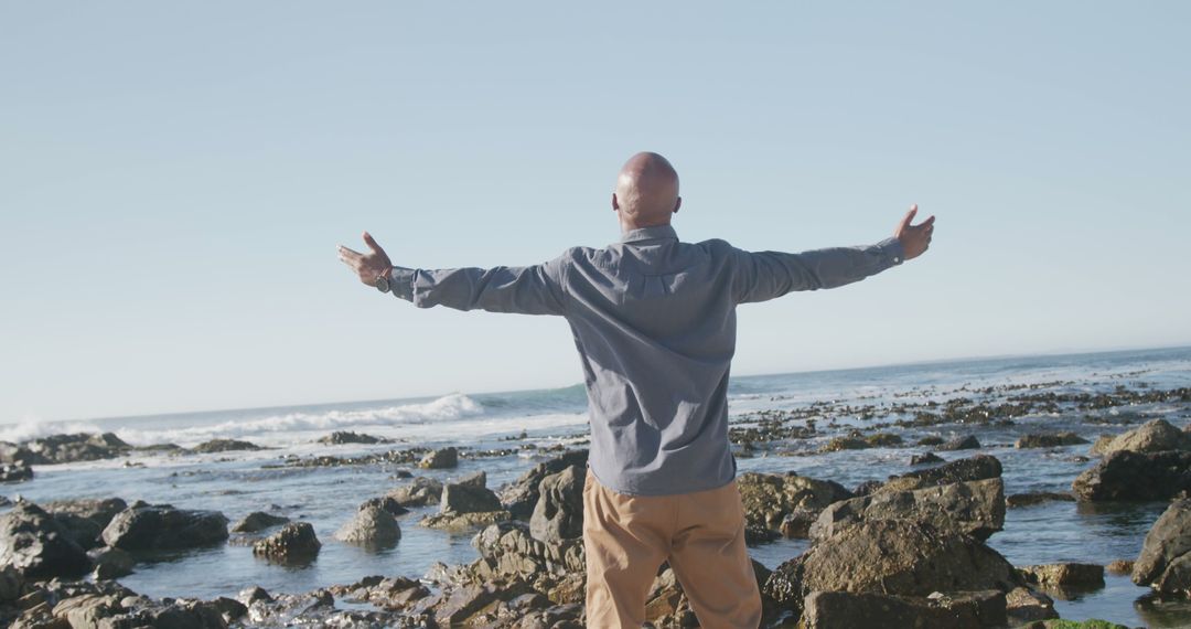 Man Embracing Nature with Open Arms Standing on Rocky Beach - Free Images, Stock Photos and Pictures on Pikwizard.com