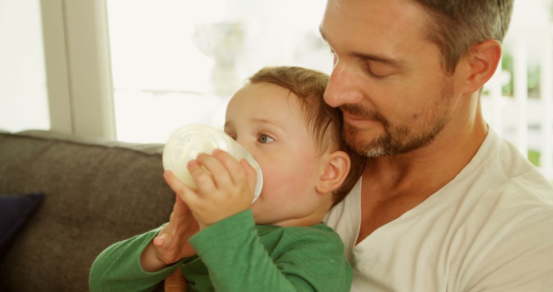 Father cuddling toddler who is drinking milk from bottle - Free Images, Stock Photos and Pictures on Pikwizard.com