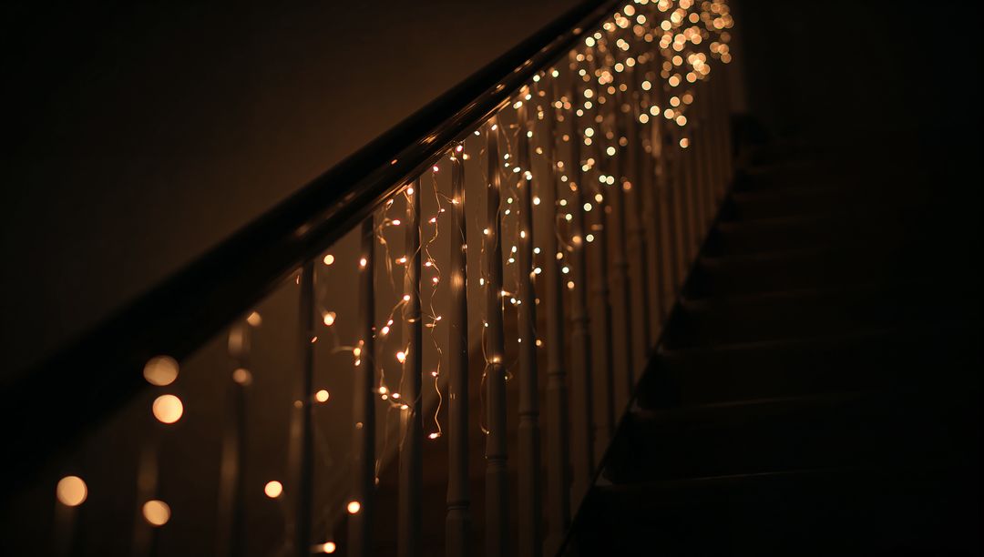 Warm fairy lights draping wooden banister with glowing bokeh and moody amber staircase