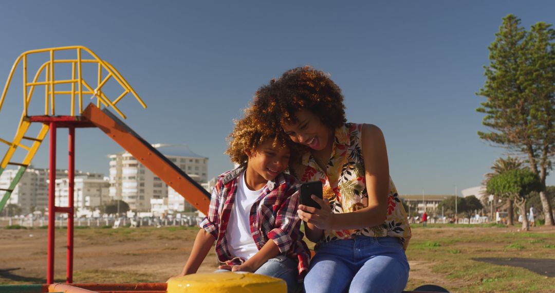 Joyful Mother and Son Bond on Sunny Playground with Smartphone - Free Images, Stock Photos and Pictures on Pikwizard.com