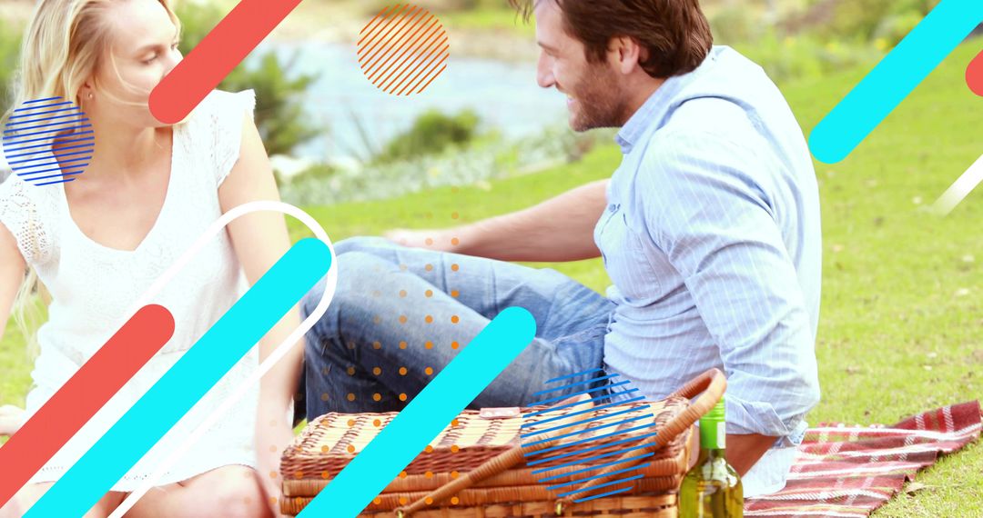 Couple enjoying lakeside picnic, chatting on blanket with wicker basket and wine bottle