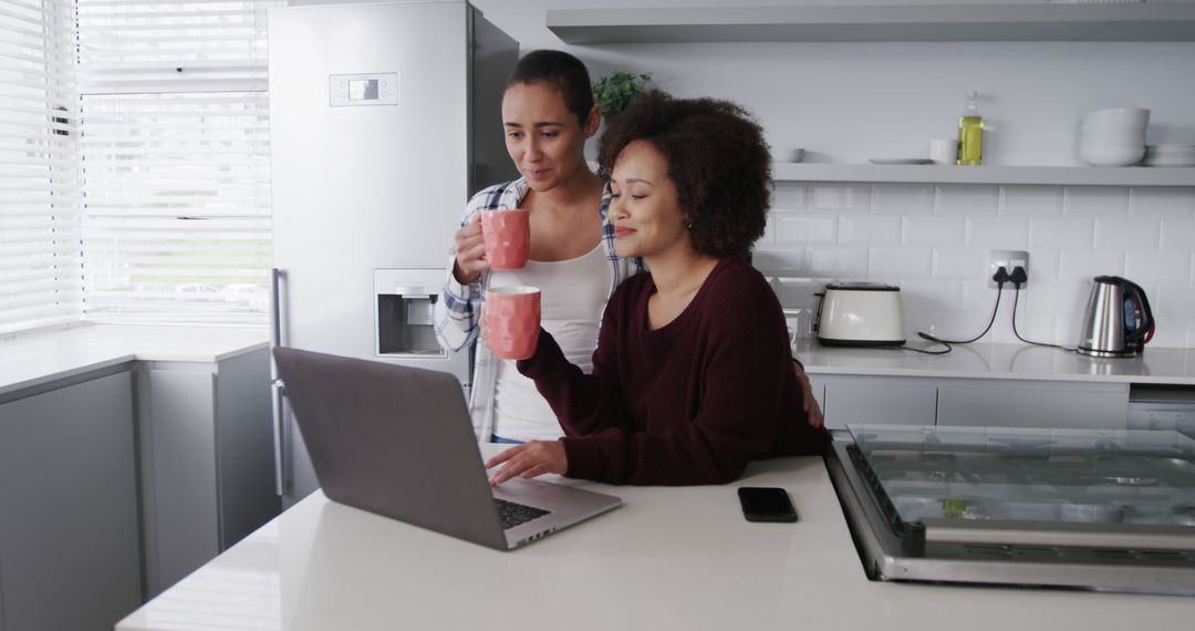 Two Women Drinking Coffee and Using Laptop in Modern Kitchen - Free Images, Stock Photos and Pictures on Pikwizard.com