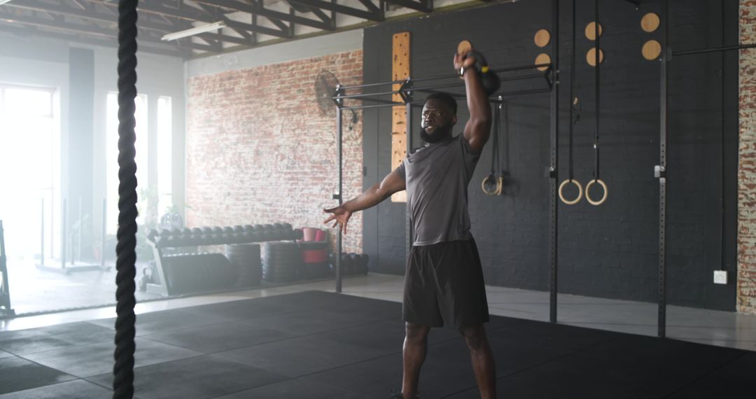 Man Performing Overhead Kettlebell Lift in Industrial Gym