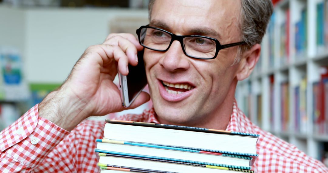 Man Holding Books Talking On Phone in Library - Free Images, Stock Photos and Pictures on Pikwizard.com