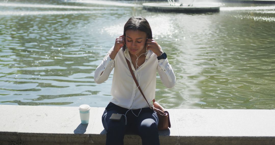 Young woman listening to music by fountain in urban park - Free Images, Stock Photos and Pictures on Pikwizard.com