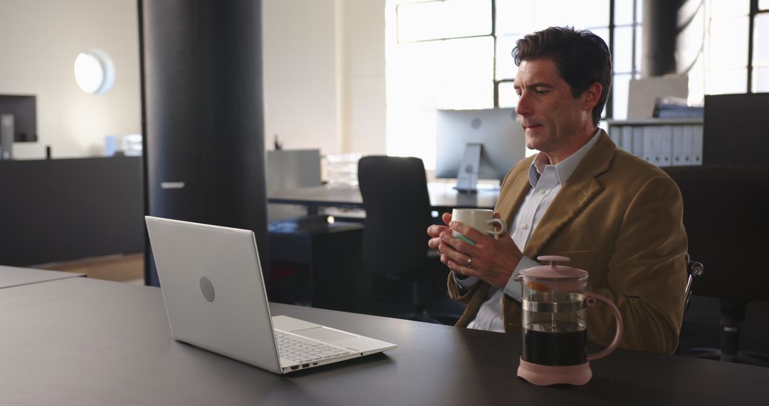 Businessperson Using Laptop Multitasking with Coffee in Office