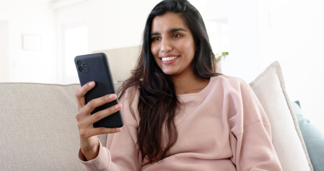 Smiling Indian Woman Relaxing on Couch with Smartphone