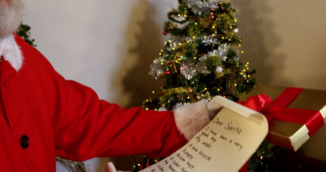 Santa Claus holding Christmas list and gift in front of decorated tree - Free Images, Stock Photos and Pictures on Pikwizard.com