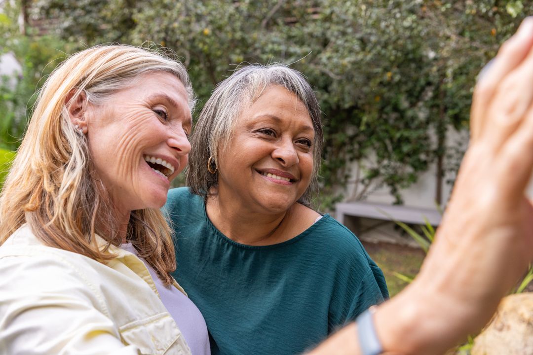 Senior Friends Smiling Together in Garden Using Smartphone