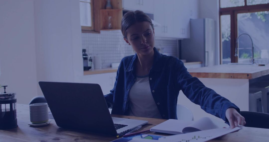 Woman Working on Laptop in Home Kitchen with Coffee and Documents