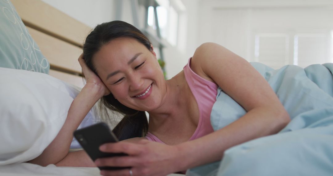 Young Woman Smiling and Texting in Bed on a Lazy Morning - Free Images, Stock Photos and Pictures on Pikwizard.com