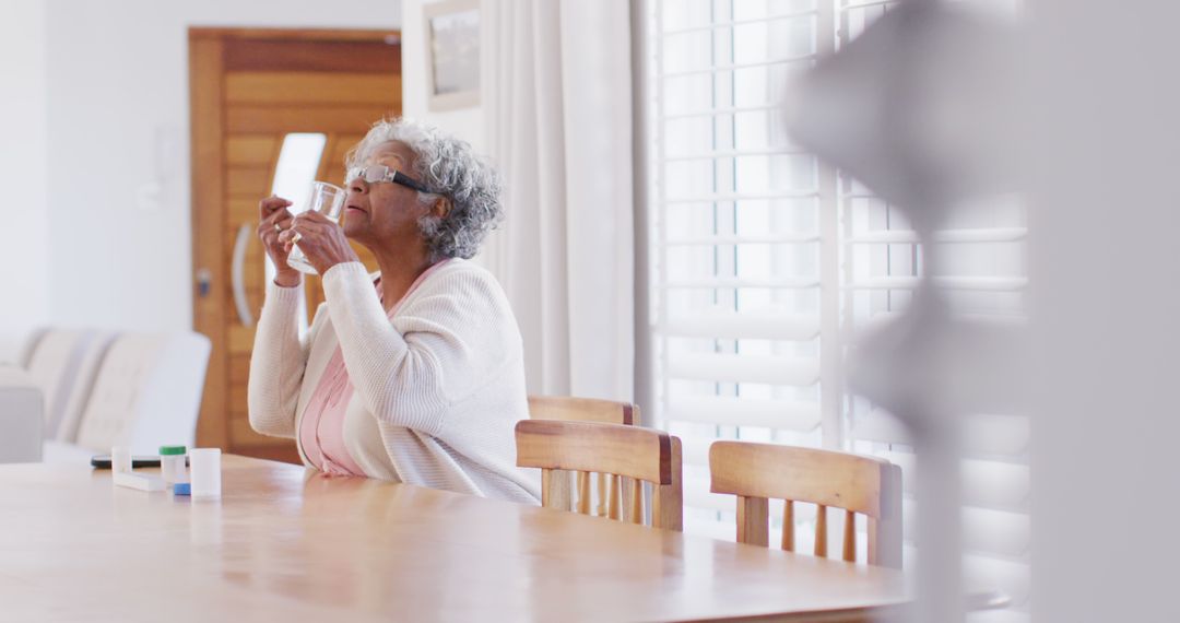 Senior african american woman sitting at table, taking pills - Free Images, Stock Photos and Pictures on Pikwizard.com